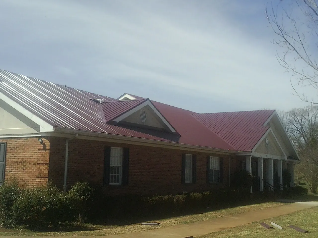 Red metal roof with gabled entries on a long brick building, from a Hail Damage Roof Repair job in Epworth