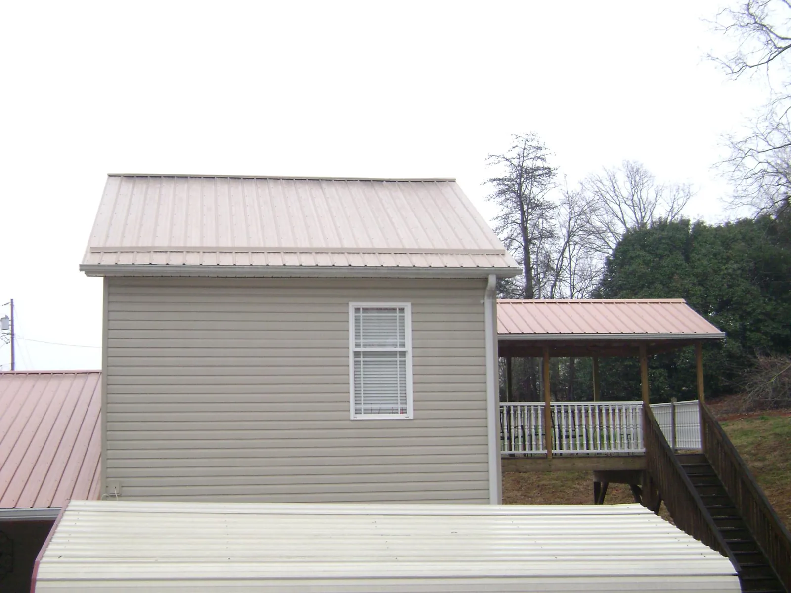 Tan metal roofs on a two story addition and attached porch, from a Roof Replacement job in Epworth